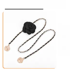 Detail of gold metal and black leather chain with large fabric camellia flower