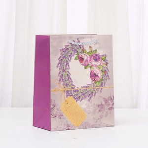 Lavendel Geschenktüte mit lila Blumenkranz-Muster und grauen Griffen auf weißem Tisch