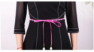 Detail of rose red velvet waist rope with pearls tied on a black dress for women