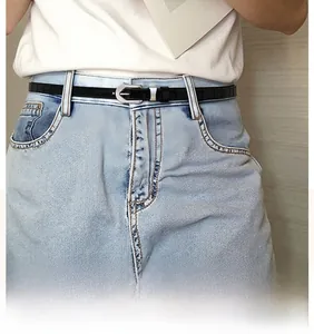 Detail view of a black crocodile pattern thin leather belt with silver buckle on blue jeans