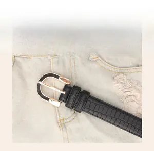 Detail of black faux crocodile leather belt with gold buckle on denim jeans