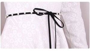 Detail of elegant black waist rope with delicate bow and pearls on white lace dress