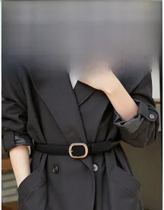 Detail of a black matte leather belt with a gold rectangular buckle on a grey wool coat