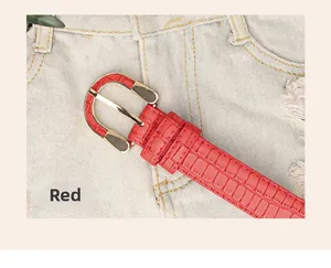 Detail shot of a red crocodile pattern leather belt with a metal buckle on light denim jeans