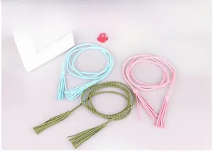 Dettaglio di cinture sottili intrecciate blu rosa e verdi con nappe decorative