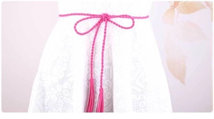 Dettaglio cintura sottile intrecciata rosa fucsia con nappe su abito in pizzo bianco