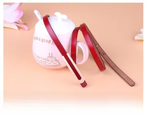 Détail d'une ceinture en cuir rouge sur une tasse en céramique avec boucle dorée en U