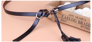 Détail d'une fine ceinture en cuir verni noir pour femme avec une boucle anneau dorée élégante