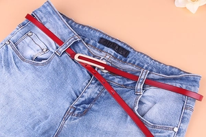Gros plan d'une fine ceinture en cuir rouge avec boucle dorée sur un jean bleu denim