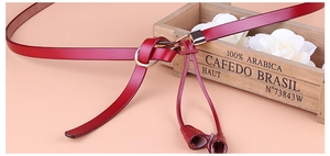 Détail de la ceinture en cuir rouge avec boucle ronde dorée et décoration de glands en cuir