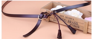 Détail de la ceinture fine en cuir marron foncé avec boucle dorée et pampille décorative