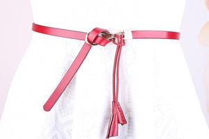 Détail d'une ceinture fine en cuir verni rouge avec boucle à crochet et effet de nœud chic