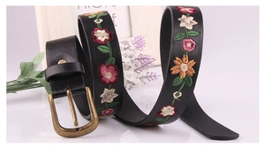 Detail shot of vintage black leather belt featuring colorful floral embroidery and bronze buckle