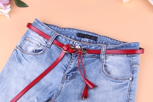 Détail d'une fine ceinture en cuir rouge avec boucle anneau argentée et pompon