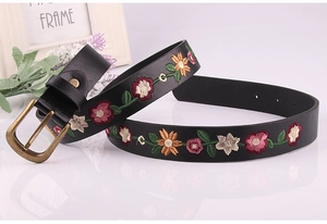 Close-up of vintage brass buckle and colorful floral embroidery on a black leather belt