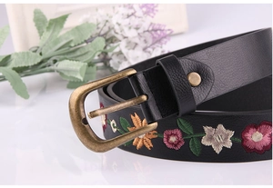 Close-up of vintage black leather belt featuring colorful floral embroidery and bronze buckle