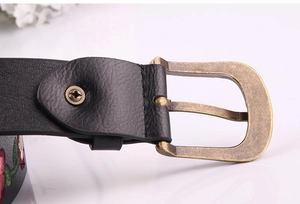 Close-up of vintage metal buckle and floral embroidery on a black faux leather belt