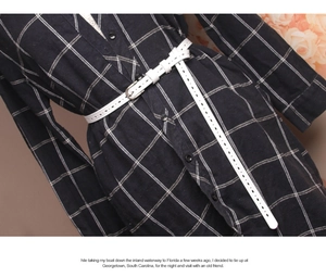 Close-up of a white leather belt with silver buckle on a navy blue plaid dress