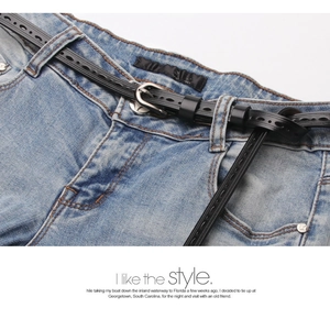 Detail of a thin black leather belt with hollow design and silver buckle on jeans
