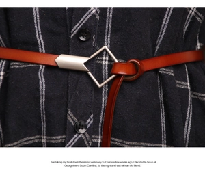 Detail of a thin brown leather belt featuring a silver geometric buckle on checkered fabric