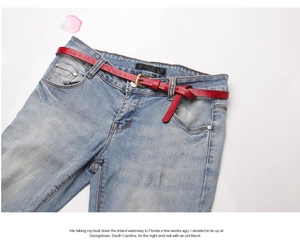 Detail of red vintage leather belt with floral embossing on washed denim jeans