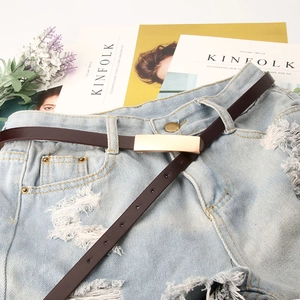 Fine ceinture en cuir marron foncé avec boucle dorée sur un short en jean bleu