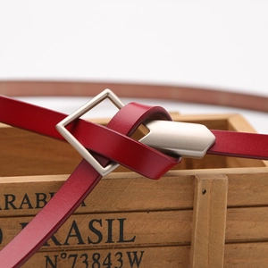 Elegant slim red leather belt for women with a matte silver square buckle on wood