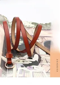 Détail d'une ceinture fine en cuir brun rouge avec boucle ronde dorée rose sur un magazine