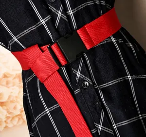Detail of red canvas belt with matte black quick-release buckle on a plaid dress