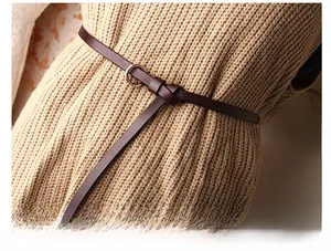 Détail de la fine ceinture en cuir marron foncé avec boucle dorée nouée sur un pull tricoté