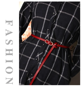Slim red leather belt with a gold oval buckle cinched over a plaid dress for a stylish look