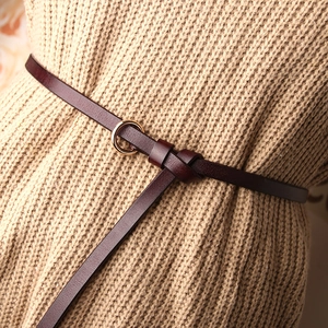 Fine ceinture en cuir pour femme avec boucle ronde dorée sur un pull en maille beige