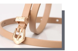 Close-up of golden vintage engraved buckle and light brown leather strap on a skinny belt