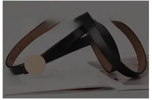 Detail of minimalist black leather belt with a polished gold circular buckle on magazines