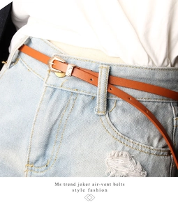 Detail of thin orange leather belt with vintage floral engraved gold metal buckle