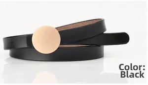 Close-up of a thin black leather belt featuring a polished round gold metallic buckle