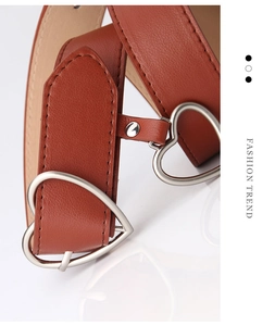 Detail of a brown leather belt featuring a matte silver heart-shaped metal buckle and stitching