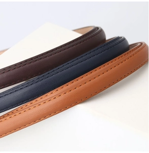 Macro detail of three thin leather belts with fine stitching in brown, navy and camel