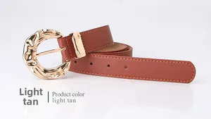 Close-up of light tan faux leather belt featuring a designer wavy gold metal buckle