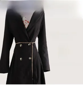 Detail of a thin gold metal waist chain on a black double-breasted coat for women