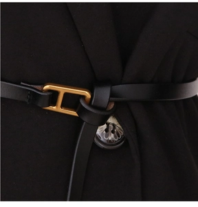 Macro close-up of a slim black leather belt featuring a polished gold H-shaped metal buckle