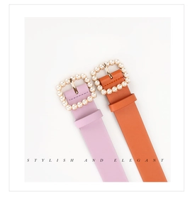 Dettaglio di fibbie quadrate dorate con perle bianche su cinture in pelle viola e arancione