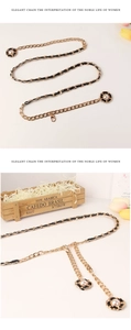 Détail d'une ceinture chaîne dorée avec cuir noir tressé et breloques de fleurs perlées