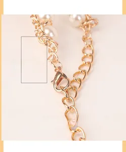 Détail d'une ceinture chaîne dorée en aluminium avec perles blanches et fermoir