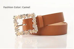 Detail of camel PU leather belt with floral rhinestone buckle on a white surface