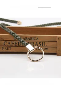 Détail d'une fine ceinture tressée vert foncé avec boucle ronde en métal doré poli