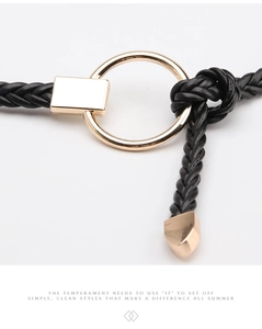 Détail d'une fine ceinture tressée noire avec boucle ronde dorée et embout métallique poli