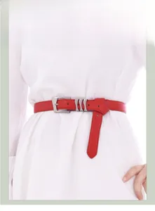 Détail d'une fine ceinture en cuir rouge avec boucles métalliques sur robe blanche