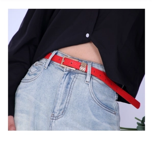 Detail of red leather belt with engraved gold buckle on light wash denim jeans