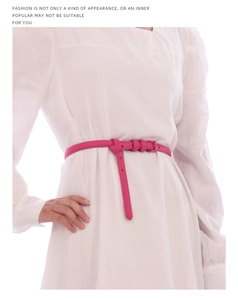 Dettaglio di una sottile cintura in pelle rosa legata con un nodo decorativo su un abito bianco